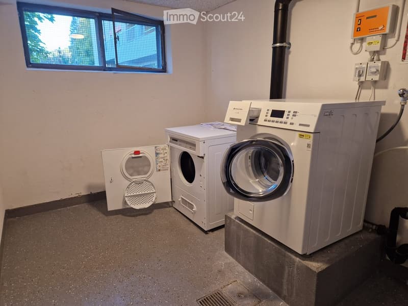 A small utility room with a washing machine, dryer, and control panel, featuring a window with a grid pattern.