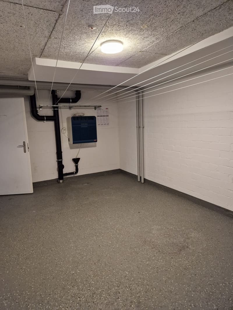 Empty utility room with white brick walls, grey concrete floor, a white door, and a blue air conditioning unit mounted on the wall.