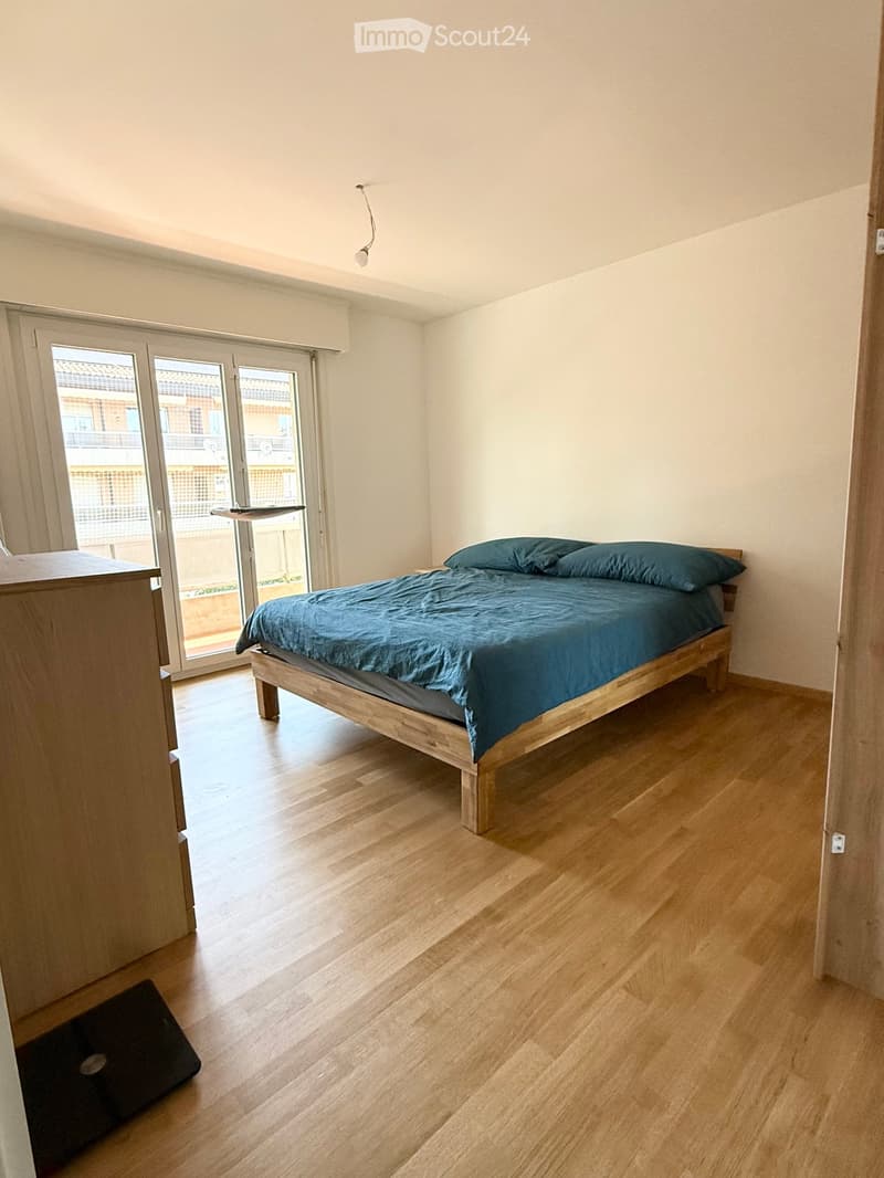 Minimalist bedroom with a wooden bed, blue bedding, and a nightstand near a large sliding glass door leading to a balcony.