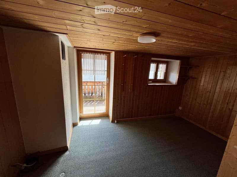 Empty room with wooden walls, carpeted floor, and a sliding glass door leading to a balcony.