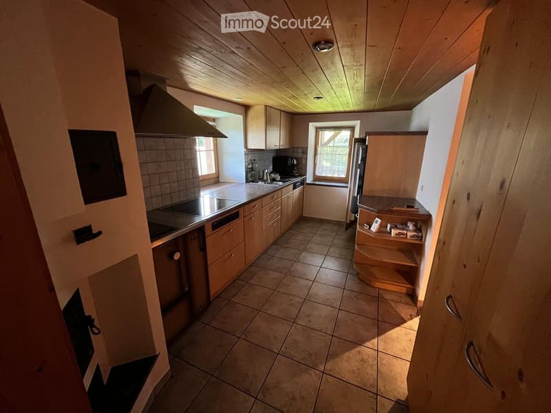Bright kitchen with wooden cabinets, tiled floor, stainless steel appliances, and natural light from windows.