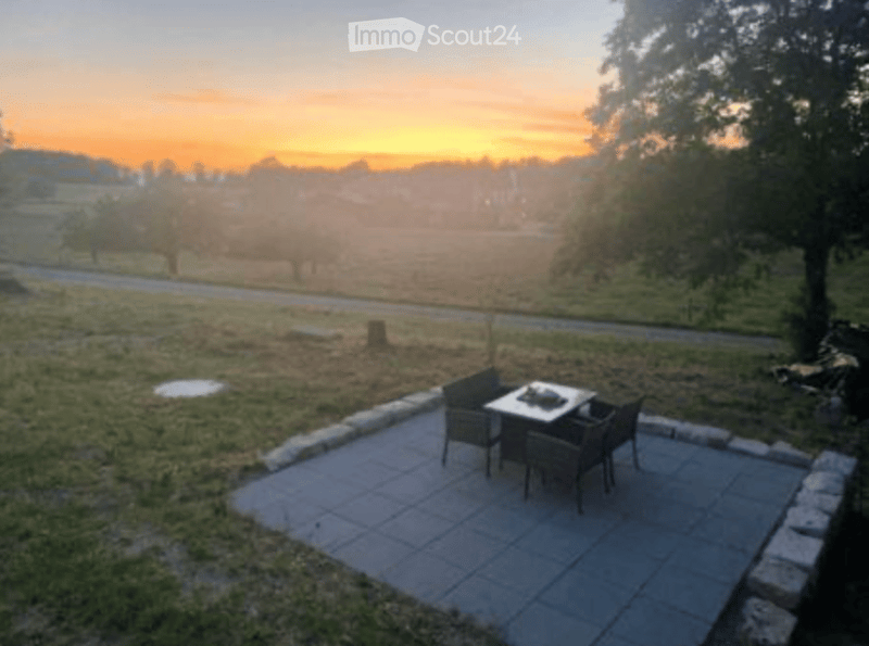 Outdoor patio with a small table and four chairs, overlooking a scenic countryside view at sunset.