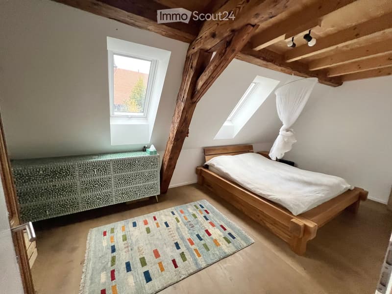 Cozy attic bedroom with wooden bed, patterned rug, dresser, and skylight windows.