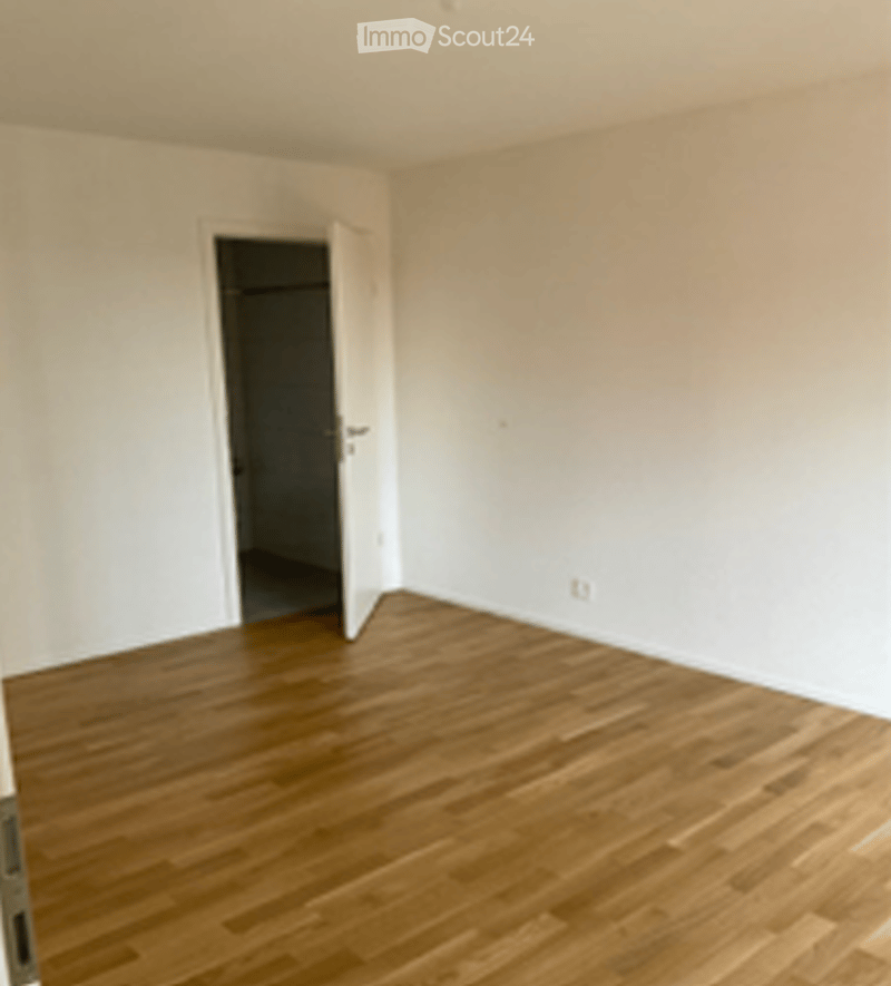 Empty room with wooden flooring and white walls, featuring an open doorway leading to another space.
