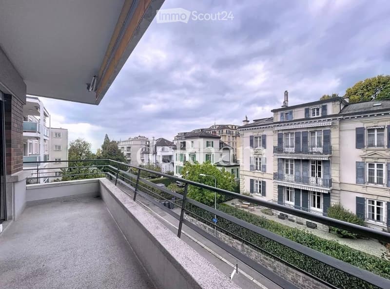 Balcony with metal railing overlooking a cityscape of residential buildings and greenery.