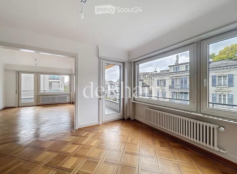Empty room with wooden flooring, large windows, and a view of the cityscape. No furniture or equipment present.