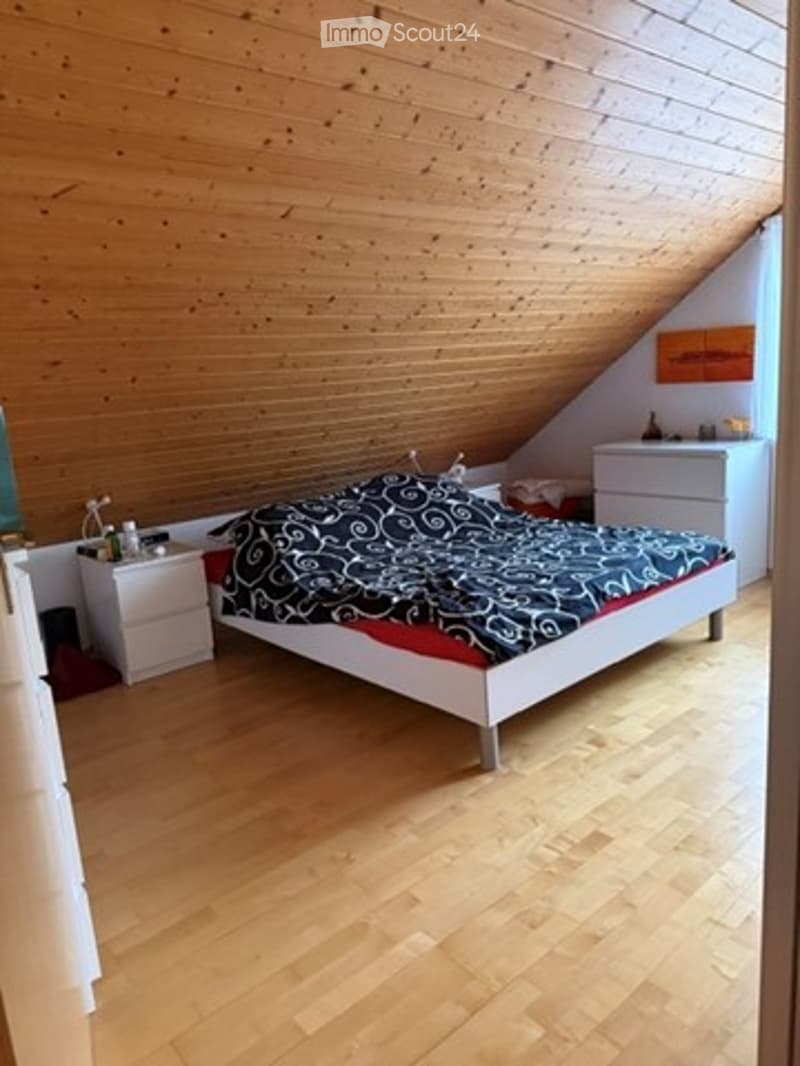 Bright bedroom with wooden walls and floor, featuring a double bed with patterned bedding, nightstands, a mirror, and a decorative painting on the wall.