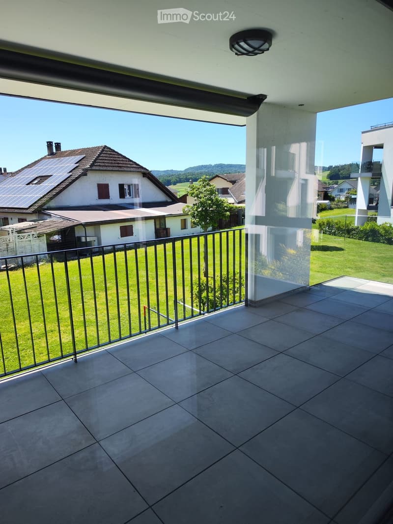 Balcony with tiled floor, metal railing, and a view of a green lawn, neighboring houses, and solar panels on a roof.