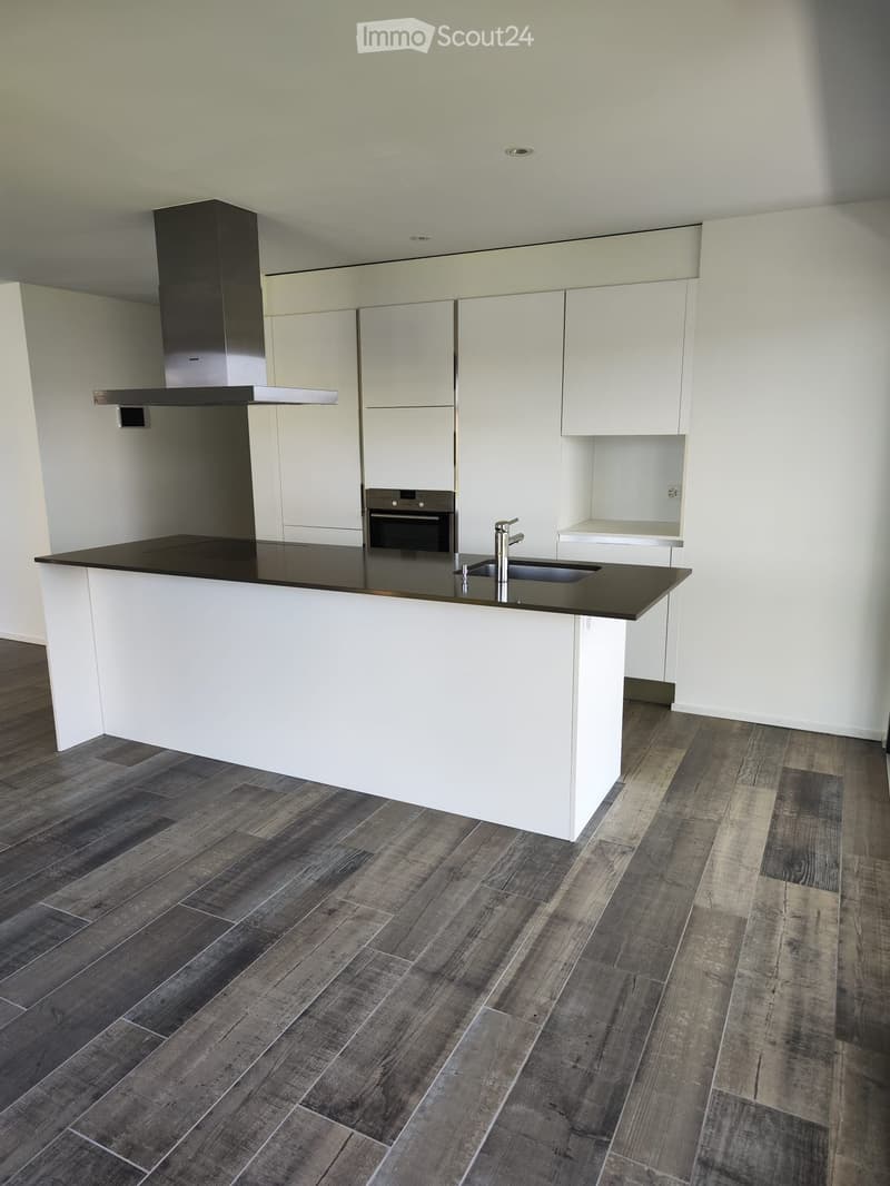 Modern kitchen with white cabinets, dark countertops, and a central island. Features include a stainless steel range hood, built-in oven, and a sink with a modern faucet.