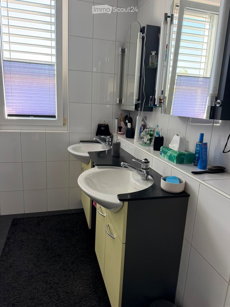 Modern bathroom with two sinks, a large mirror, and various toiletries neatly arranged on the counter.
