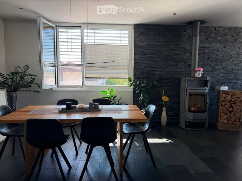 Modern dining area with a wooden table, black chairs, a sleek fireplace, and decorative plants.