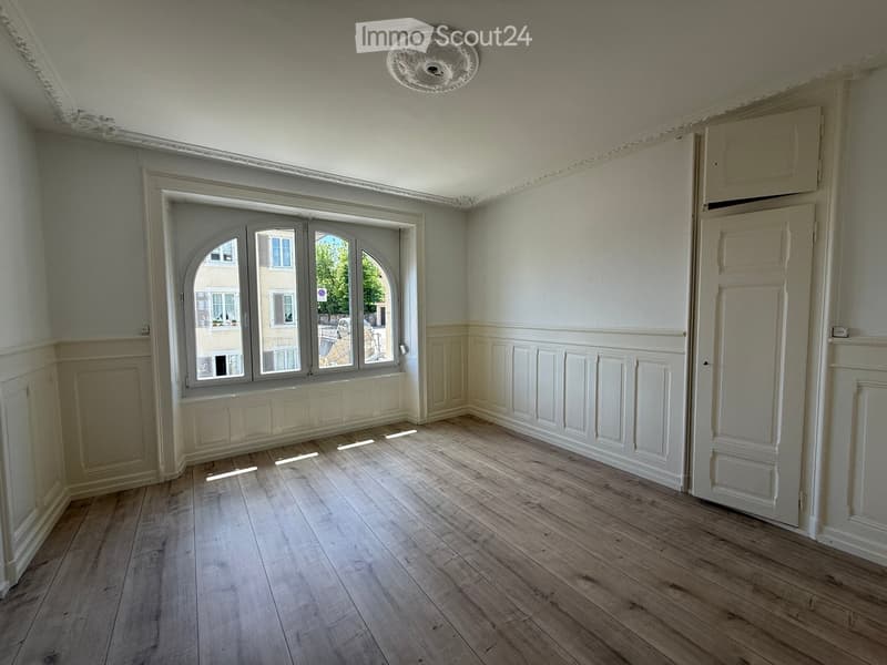 Empty room with wooden flooring, white walls, large arched window, and decorative molding.