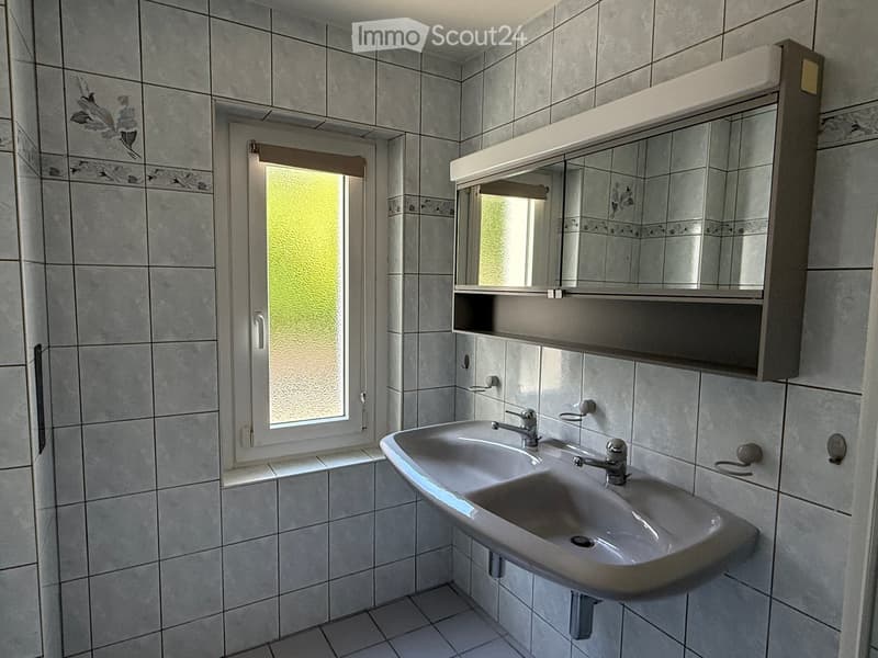 Bathroom with a double sink, mirror cabinet, and frosted window. Grey tiled walls and floor.