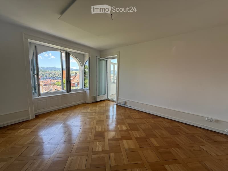 Empty room with wooden flooring, large arched windows, and white walls. No furniture or equipment present.
