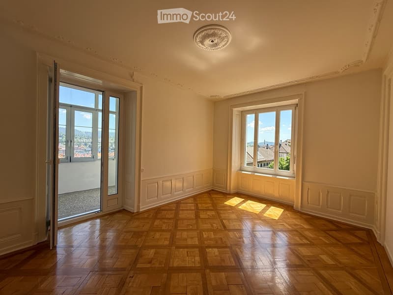 Empty room with wooden parquet flooring, large windows, and a balcony door leading to a view of the city.