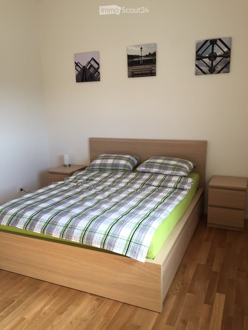 A neatly arranged bedroom with a wooden bed, plaid bedding, two nightstands, and wall art.