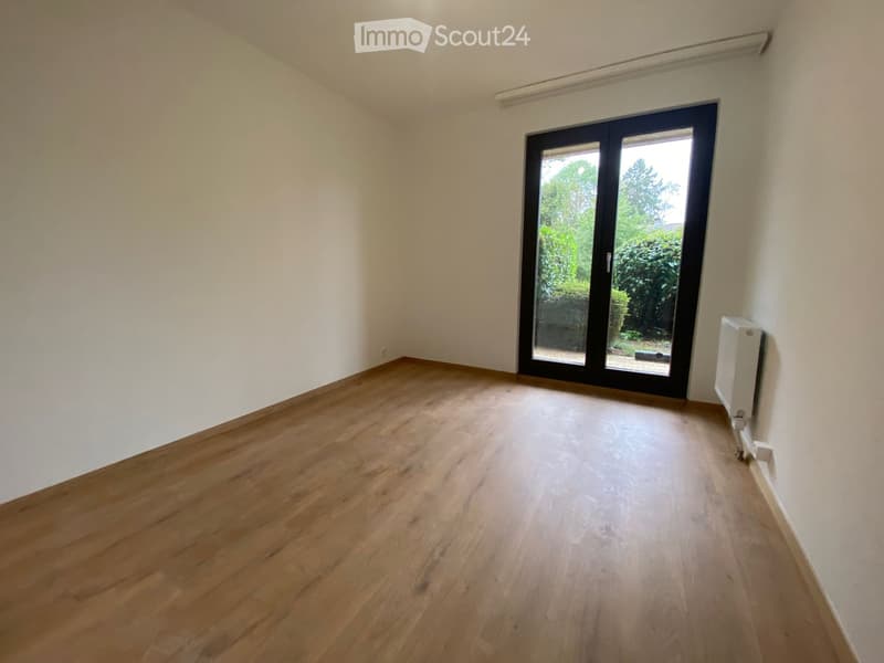 Empty room with wooden flooring, white walls, and a large sliding glass door leading to an outdoor area.