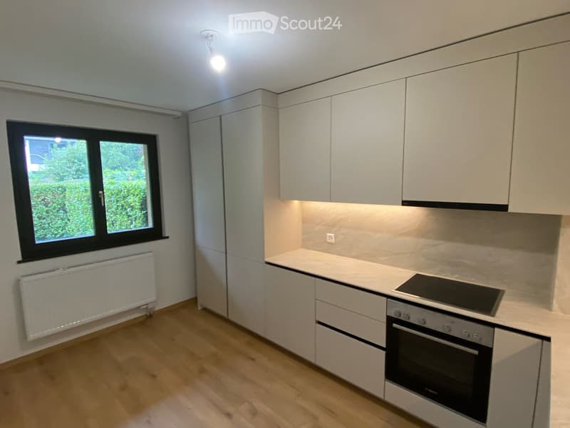 Modern kitchen with white cabinets, a built-in oven, a stove, and a radiator under a window.