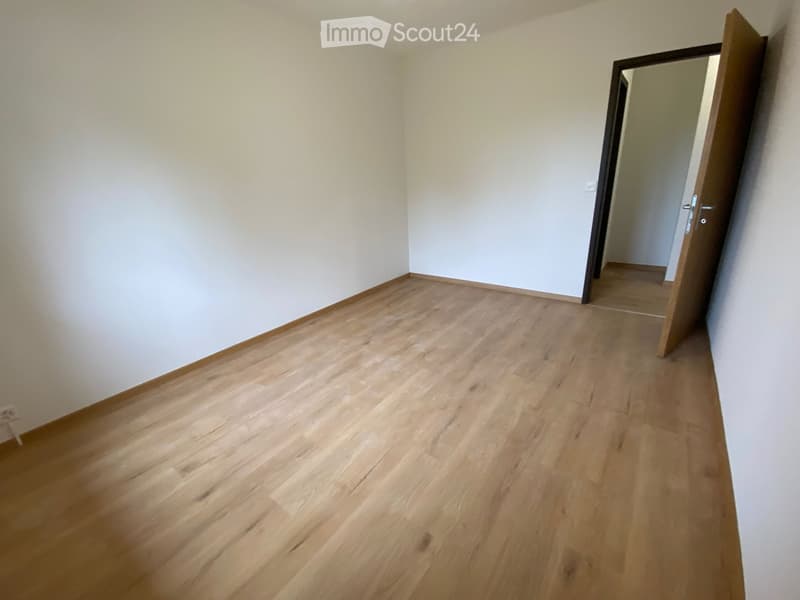 Empty room with light wooden flooring and white walls, featuring an open doorway leading to another space.