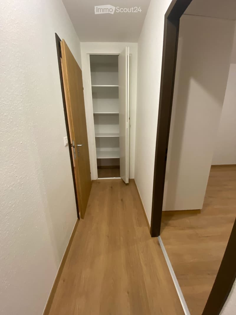 Empty hallway with wooden flooring, white walls, and open closet with empty shelves.
