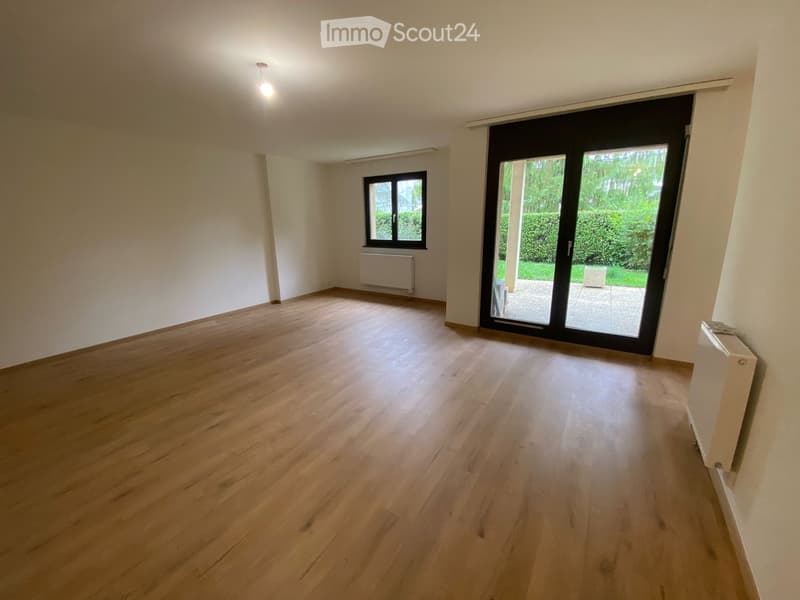 Empty room with wooden flooring, white walls, and large sliding glass doors leading to a garden area.