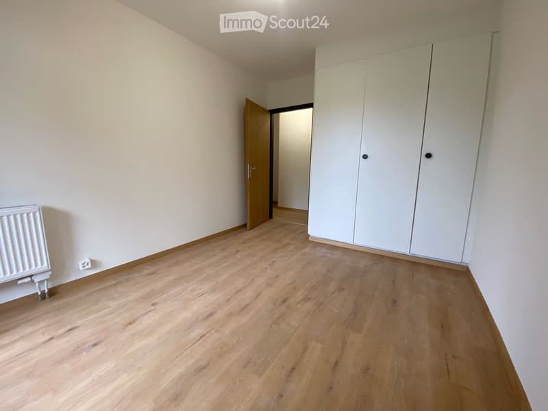 Empty room with light wooden flooring, white walls, a built-in white wardrobe, and a radiator on the left side.