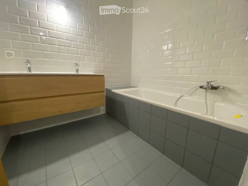 Modern bathroom with white brick walls, a wooden vanity, a bathtub, and tiled flooring.