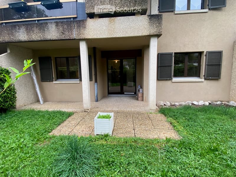 Front yard with grass, small planter, and entrance to a two-story building with windows and a balcony.