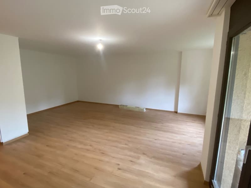 Empty room with wooden flooring and white walls, featuring a large window and a door leading outside.