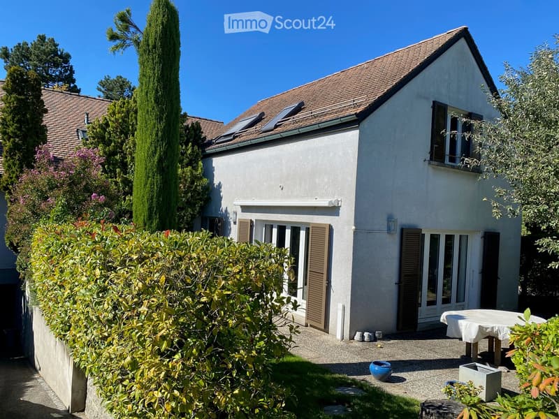A modern two-story house with a well-maintained garden area featuring a table, potted plants, and a blue decorative bowl.