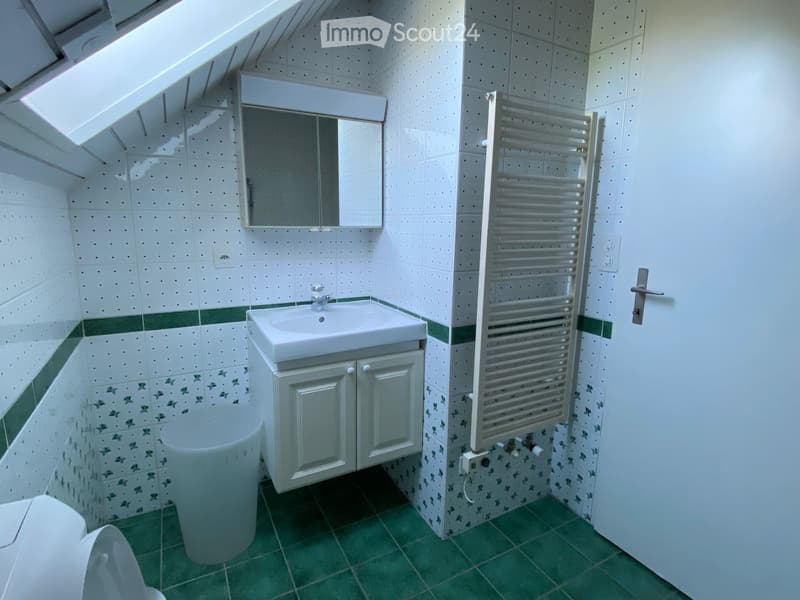 Small bathroom with white tiles, green accents, a sink with a mirror, a radiator, and a toilet.