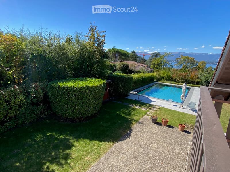 Well-maintained garden with a swimming pool, surrounded by greenery and a clear view of the lake and mountains.