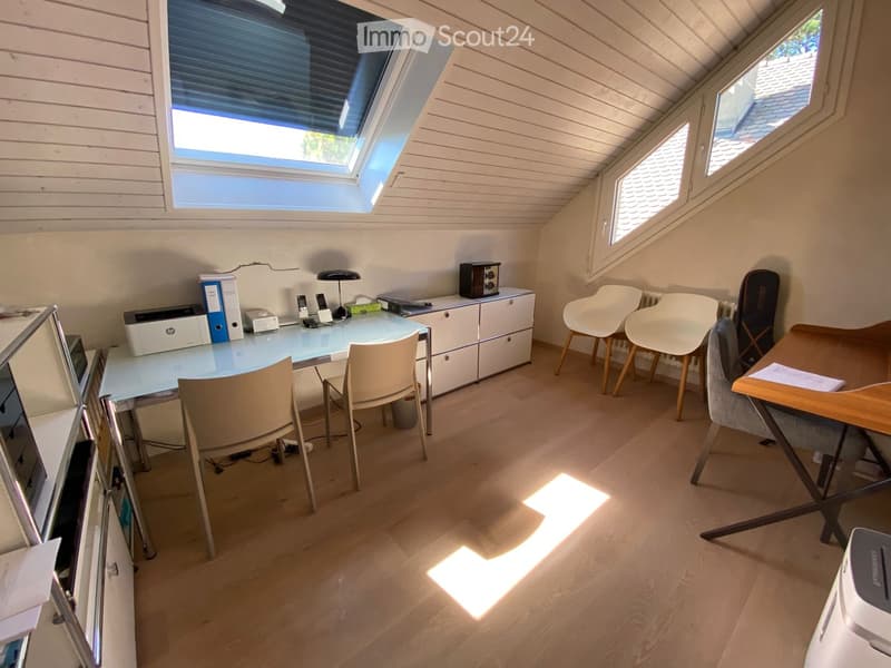 Bright attic room with wooden flooring, large skylight windows, and modern furniture including a desk, chairs, and a printer.