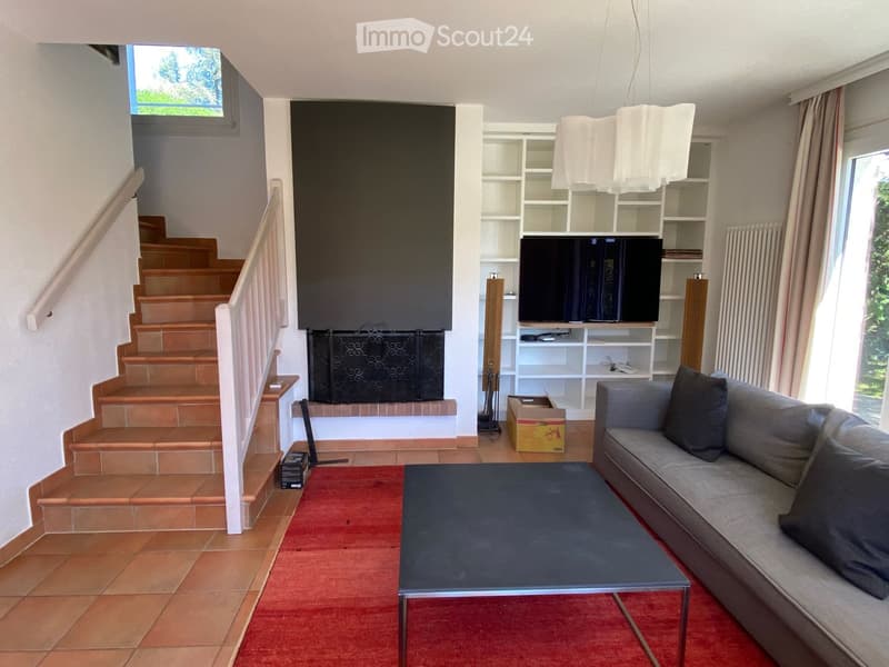 Living room with a grey sofa, black coffee table, television on a white shelf, fireplace, and a staircase leading upwards.