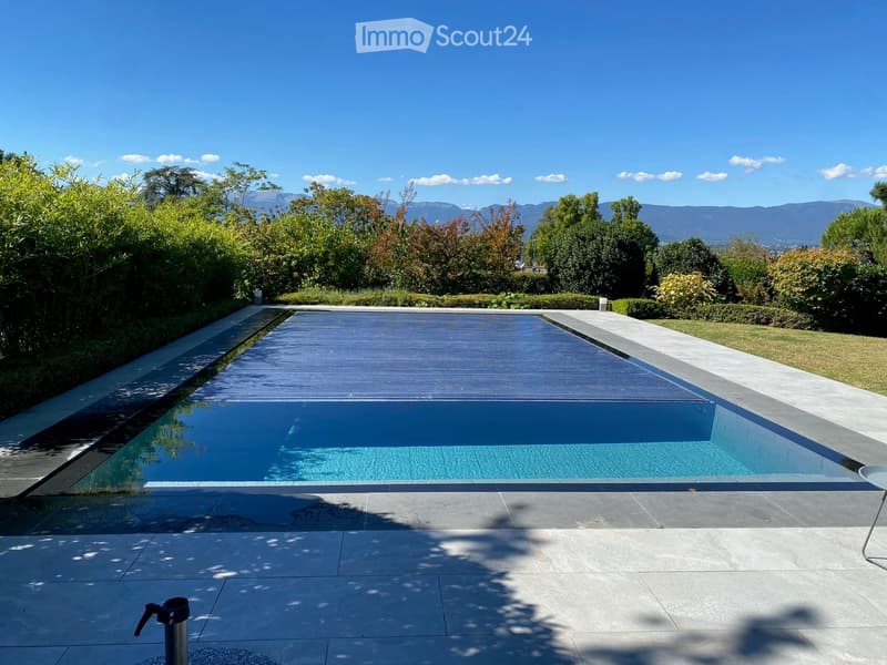 A modern rectangular swimming pool with a sleek design, surrounded by neatly trimmed hedges and lush greenery, with a scenic mountain view in the background.