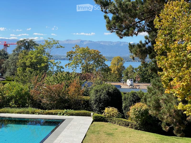 Lush garden with a swimming pool, neatly trimmed hedges, and a scenic view of mountains and a lake in the background.