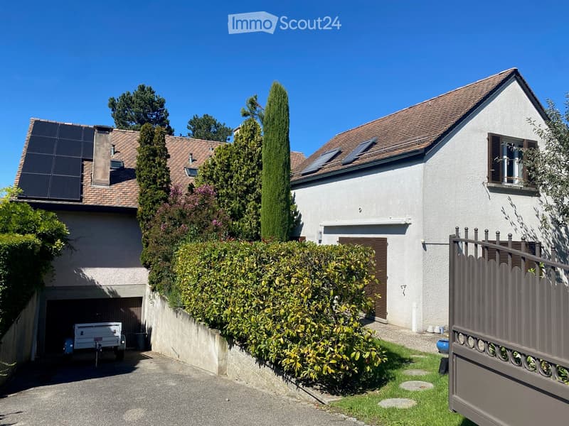 Two-story house with a tiled roof, solar panels, garage, and well-maintained garden with a hedge and gate.