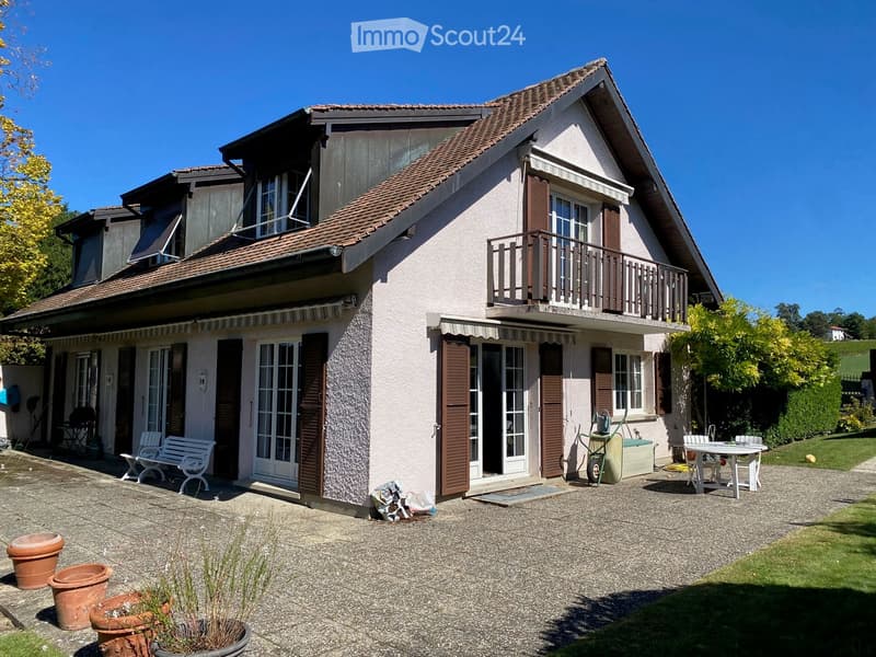 Two-story house with a balcony, multiple windows, and a well-maintained garden area with outdoor furniture and potted plants.