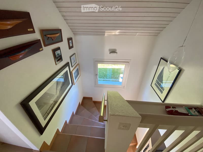 Spiral staircase with wooden steps, white walls, framed artwork, and a hanging light fixture.
