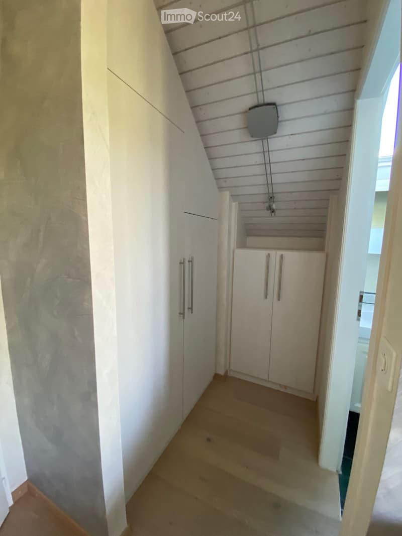 Narrow hallway with wooden flooring, white walls, built-in storage cabinets, and a small window at the end.