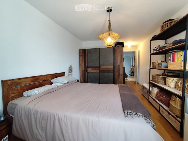 Cozy bedroom with wooden bed, white bedding, a large wardrobe, and a shelving unit with baskets and books.