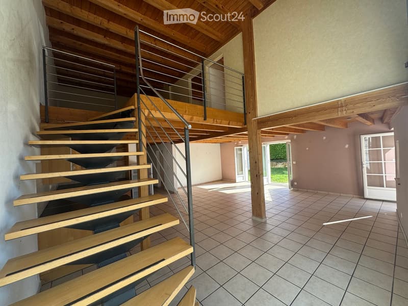 Spacious hallway with wooden staircase leading to an upper level, tiled floor, and large glass doors opening to an outdoor area.