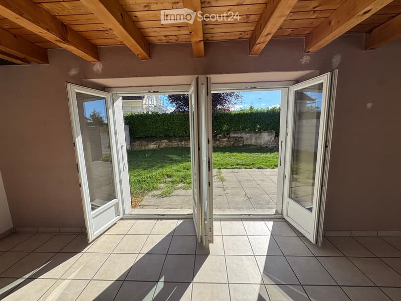Empty room with tiled floor and large sliding glass doors leading to a garden area.