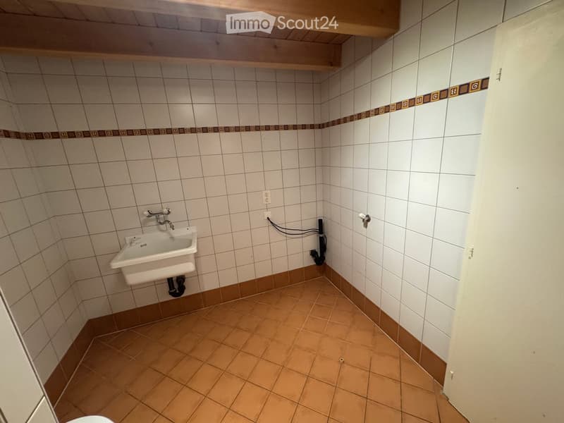 Small bathroom with white tiled walls, brown tiled floor, and a single sink with a faucet.