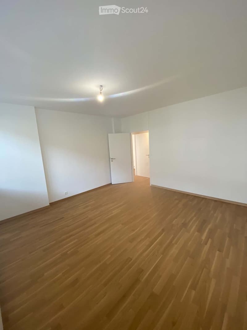 Empty room with wooden flooring, white walls, and a single door leading to another space.