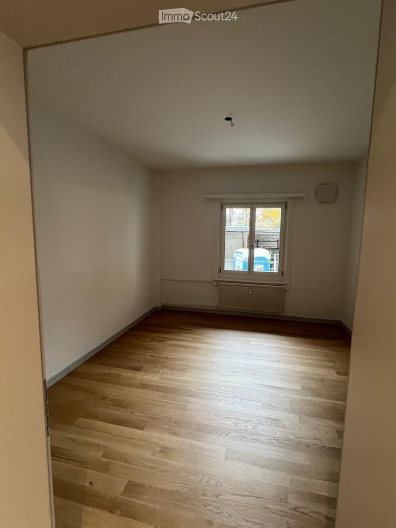 Empty room with wooden flooring, white walls, and a window with a radiator below it.