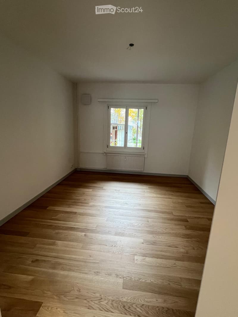 Empty room with wooden flooring, white walls, and a single window with a radiator below it.