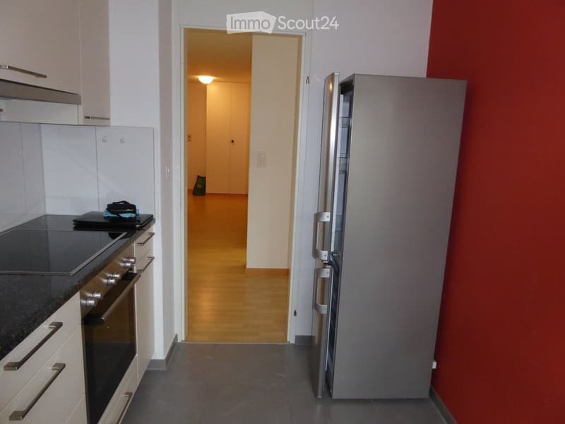 Modern kitchen with white cabinets, stainless steel appliances, and a dark countertop. A hallway leads to another room.