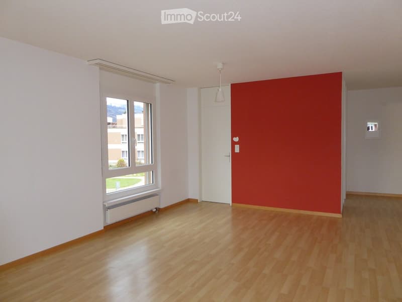 Empty room with wooden flooring, white walls, large window, and a red accent wall. No furniture or equipment present.