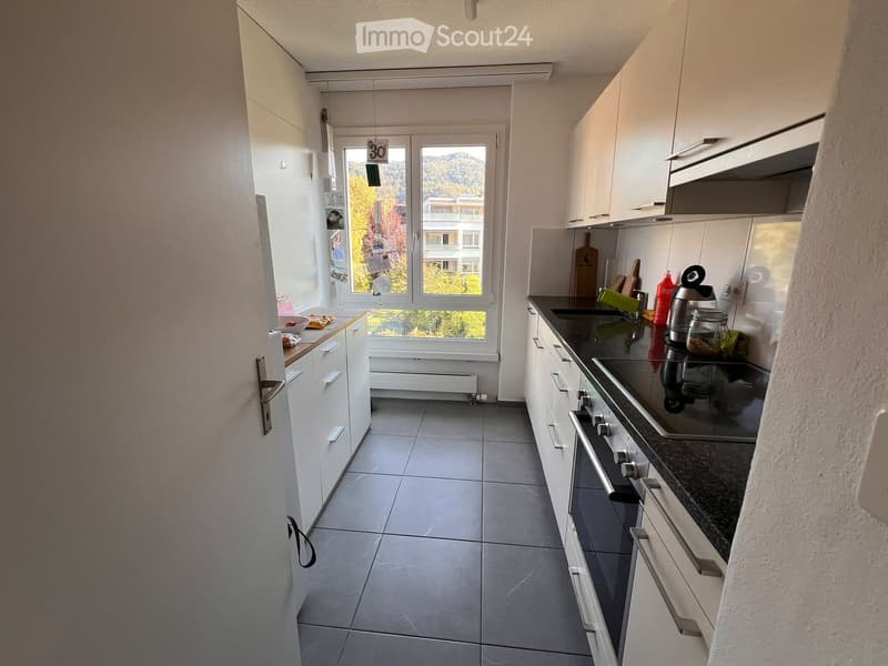 Modern kitchen with white cabinets, dark countertops, and stainless steel appliances. Features an oven, stove, and various kitchen items on the counter.
